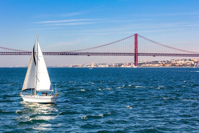 Sailboat close to April 25th Bridge over the Tagus river, Lisbon, Portugal